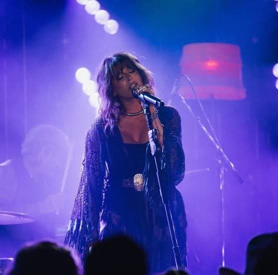 Ella Langley at the microphone in a dark lace kimono, lit blue and purple with the crowd silhouetted in front of her